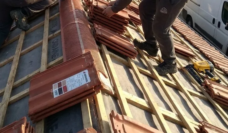 Gros plan sur les tuiles mécaniques rouges et les liteaux d'un toit en cours de couverture à Firminy